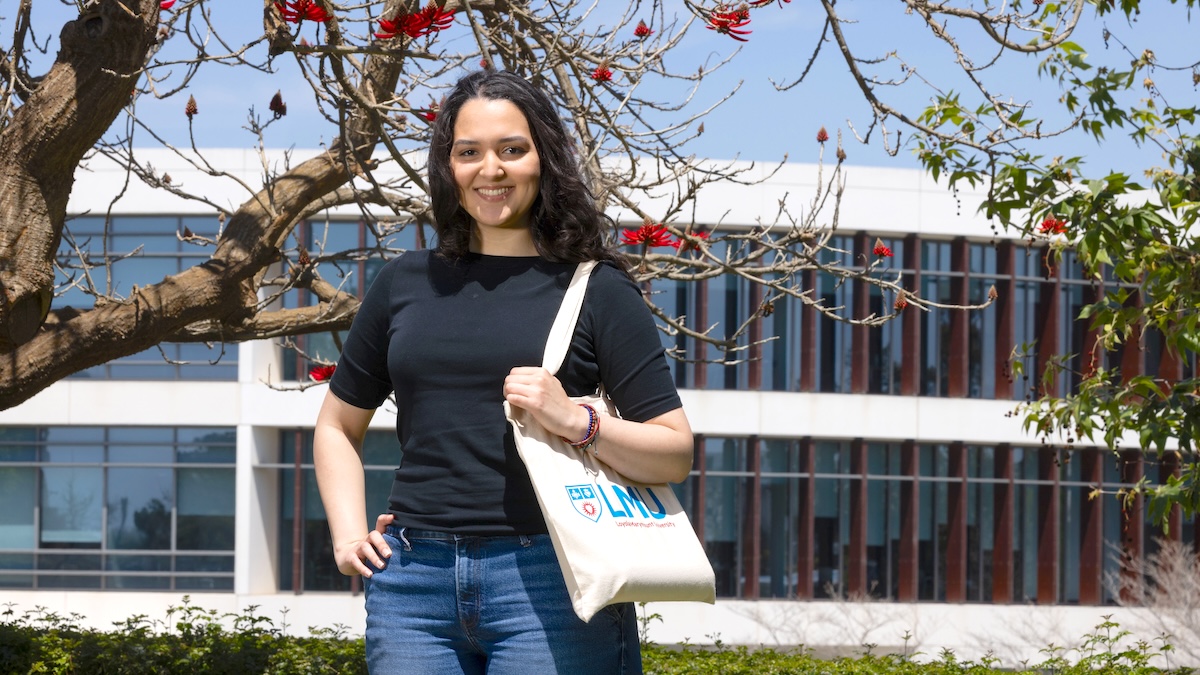 Student standing in front of library with a tote bag in her hand.